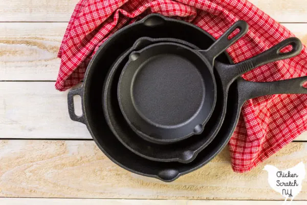 Stack of cast iron skillets on a wooden cutting board with a red checked dish towel 