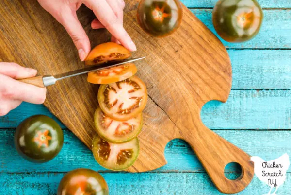 Knife cutting heirloom tomatoes on an aged wooden butting board on a blue table 