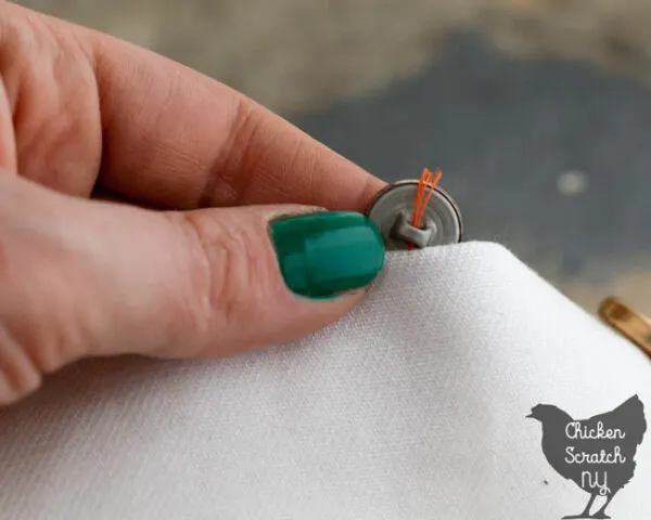 hand sewing a shank button to while fabric with orange thread 