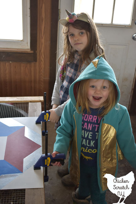 two girls using clamps to hold a piece of sheet metal against a piece of wood