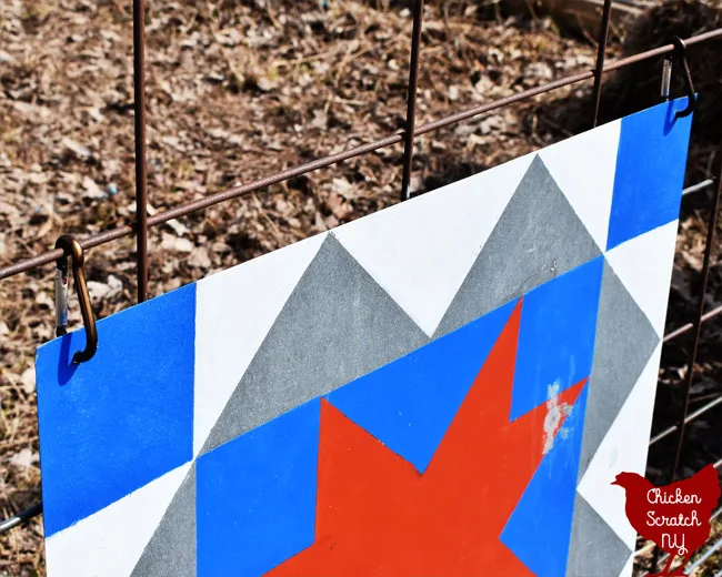 two carabiner clips holdin a sheet metal barn quilt to a cattle panel gate