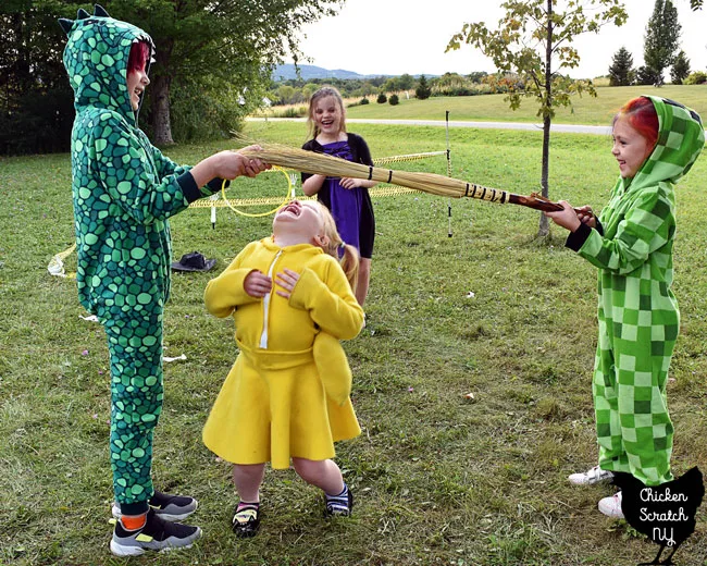 four kids in Halloween costumes playing limbo with a broom stick at a party