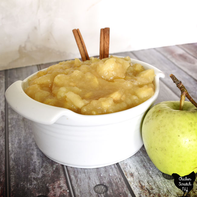white ceramic bowl willed with warm chunky applesauce made with maple syrup and fall spices with a green apple