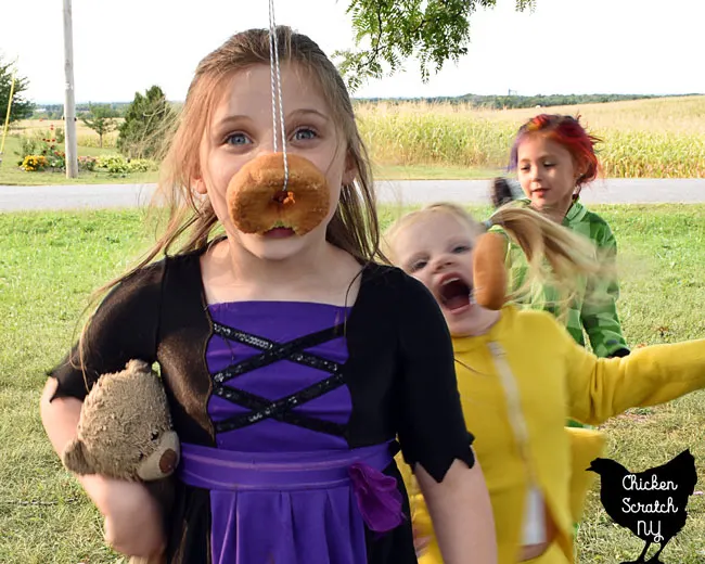 child in witch Halloween Costume playing donut on a string party game