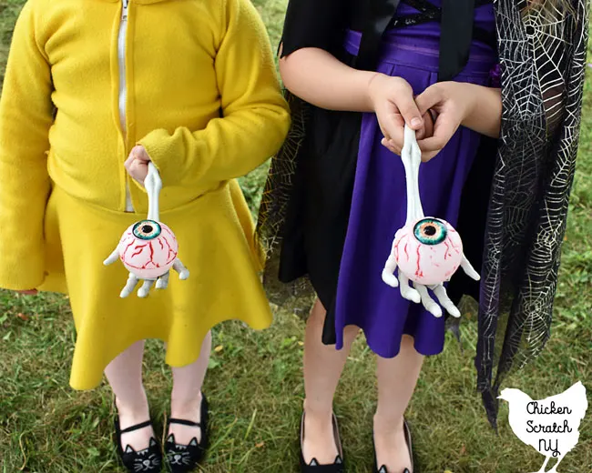two girls in Pikachu and witch costumes holding plastic eyeballs on skeleton hands for a Halloween Party egg race