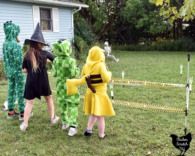 four kids in costumes playinf Skelton Ring toss Halloween party game with skeleton hand lawn stakes and glow ring necklaces