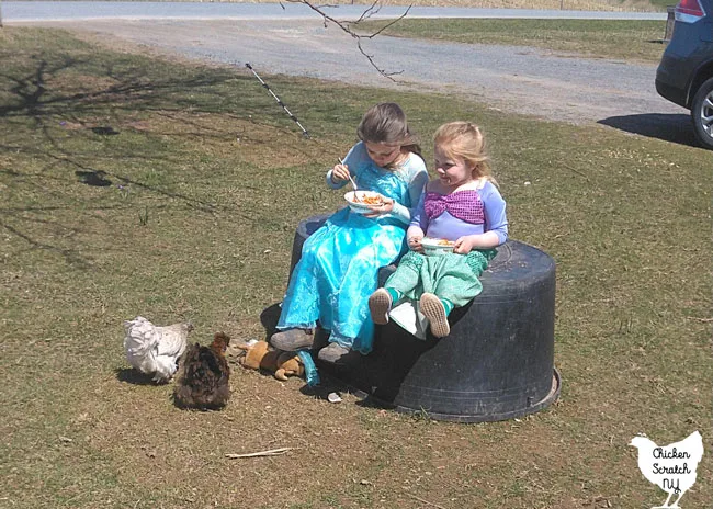 two girls in princess dresses eating spaghetti with two pet chickens