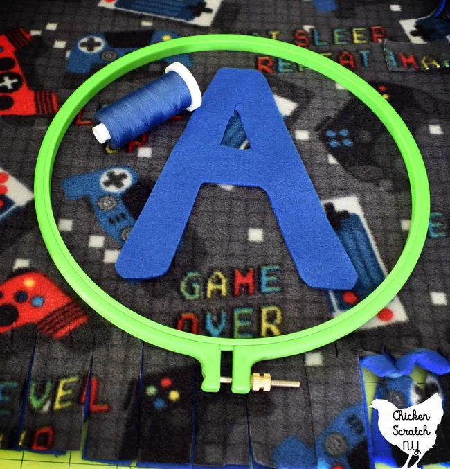 blue fleece A in an embroidery hoop laying over a gamer fleece print with a spool of blue thread