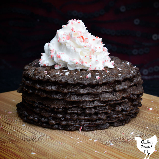 chocolate peppermint icebox cake with whipped cream and crushed candy canes on a wooden cutting board