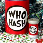 standard sized tin can with black, red and white "Who Hash" label next to a wooden spool with matching label on a red, green and white paper with sparkly tinsel background with text over lay "How the Grinch Stole Christmas Who Hash Decorations"