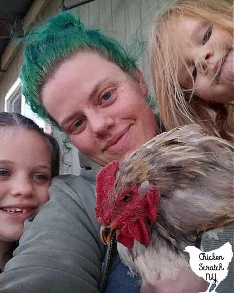 adult woman with green hair holding a large grey cochin rooster sitting with two children