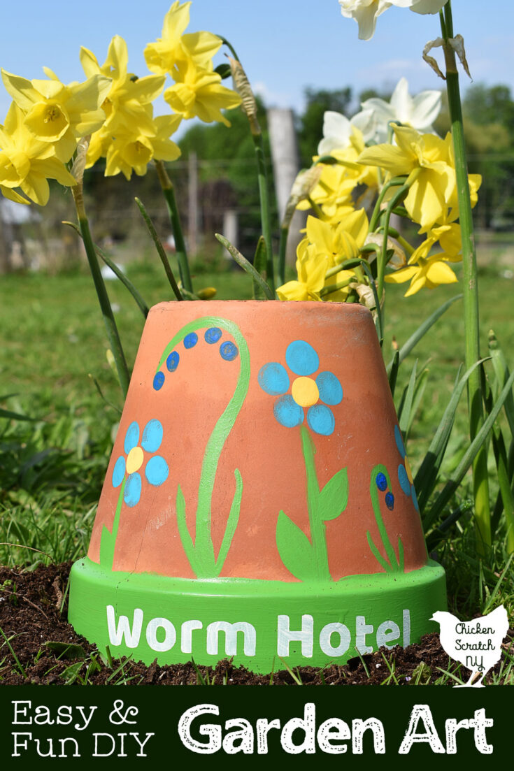 upturned flower pot with hand painted flowers and text " worm hotel" painted on the brim sitting in garden soil with yellow and white daffodils in the background with text overlay" Easy & Fun DIY Garden Art"