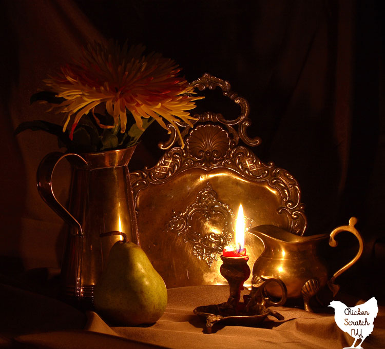 still life with metal tray, pear, vase with sunflowers and lit candle 