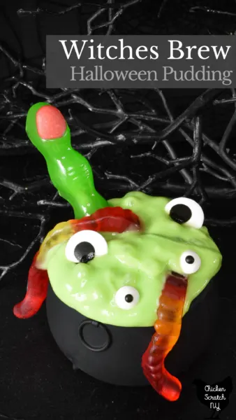 black cauldron filled with green tapioca pudding decorated with halloween finger lollipop, gummy worms and candy eyeballs