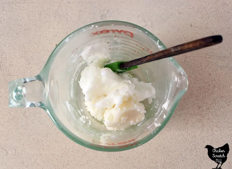 solid mango and shea butter in a glass measuring cup with a spatula