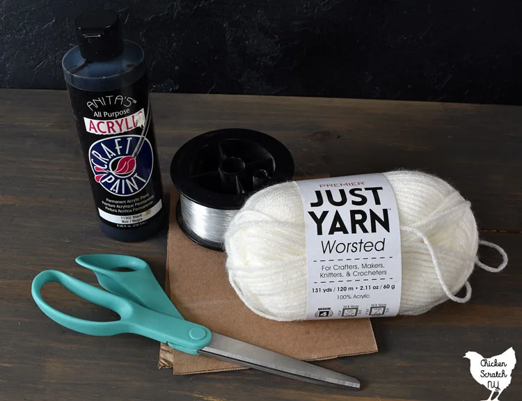 yarn ghost supplies including white dollar tree yarn, fishing line, black craft paint, scissors and cardboard template