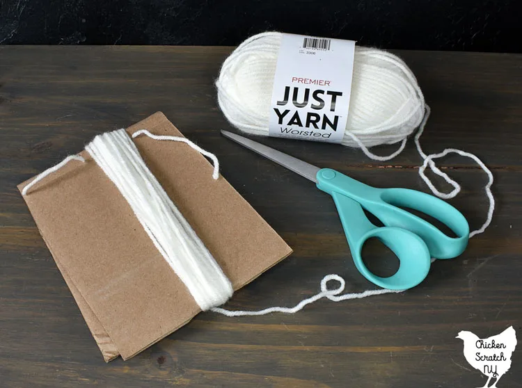 cardboard template for making a yarn tassel ghost with white yarn and a pair of scissors 
