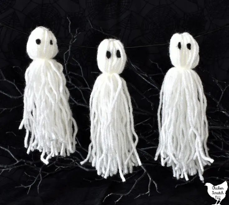 trio of white ghosts made from yarn with painted eyes hanging on fishing line