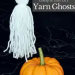 single white yarn ghost hanging from fishing line with a small orange pumpkin