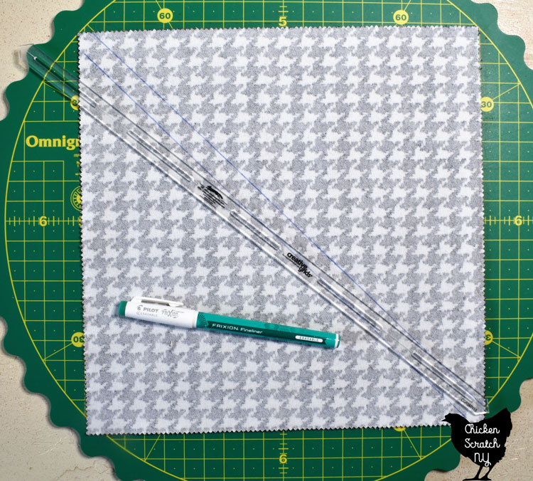 10" fabric square laying on a rotating cutting mat with a 1/2 inch ruler and a green frixion pen