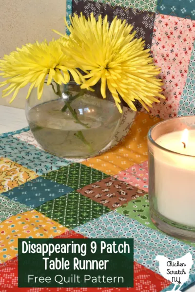 disappearing nine patch table runner made with Lori Holt Stitch fabric with a vase holding two yellow spider mums and a lit candle with text overlay "Disappearing 9 patch table runner free quilt pattern"
