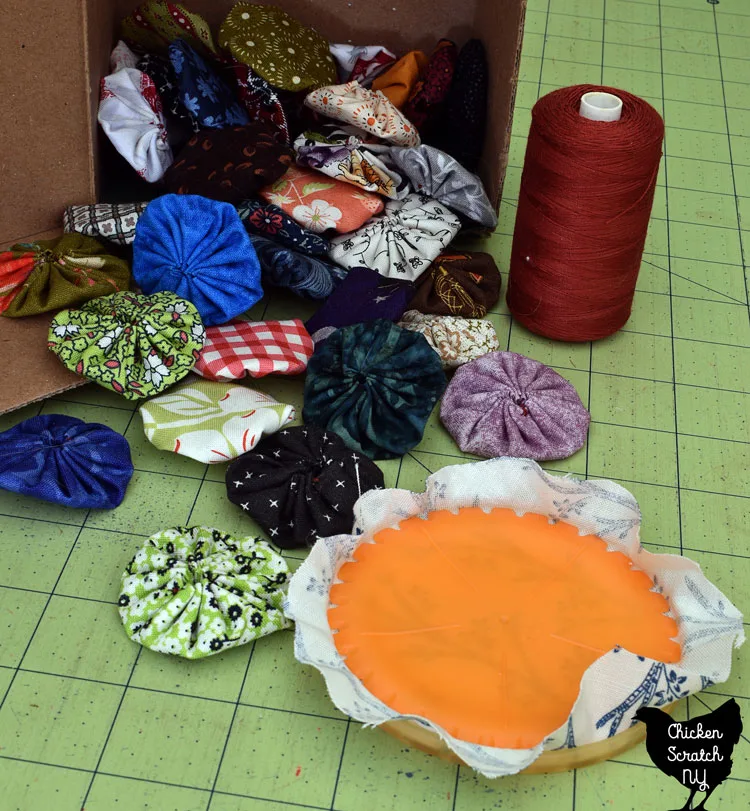 fabric yo-yos in multiple colorful fabrics  made with orange clover yo-yo maker shown with blue and white fabric sandwiched between disks