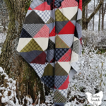 cozy corners quilt sewn with red, green, cream and gray flannel displayed in a tree surrounded by snow with text overlay "cozy corners layer cake quilt pattern"