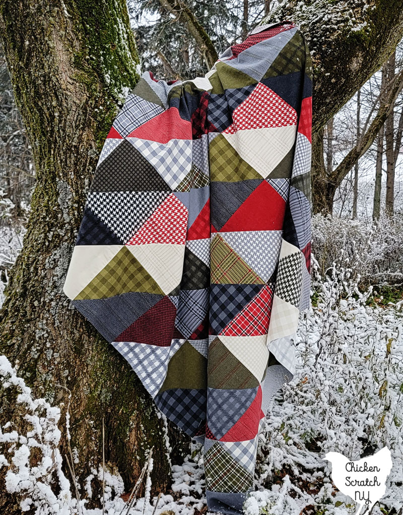 cozy corners layer cake quilt made from red, greeb, gray and cream flannel prints hanging in a tree surrounded by snow