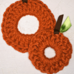 two crocheted pumpkin scrunchies with ribbon stems and leaves