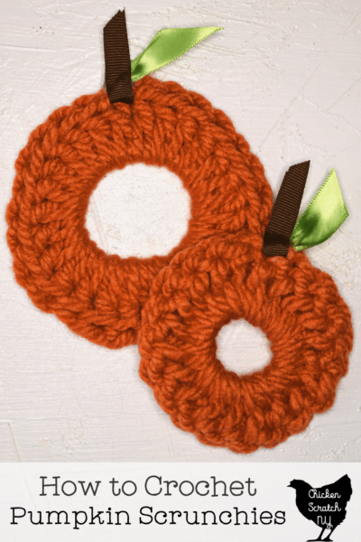 two crocheted pumpkin scrunchies with ribbon stems and leaves