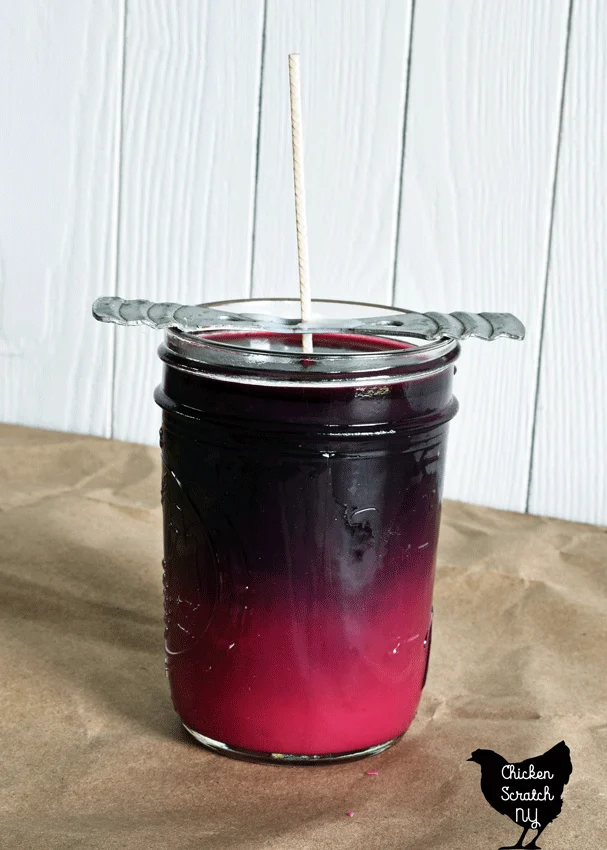 recently poured soy wax jar candle with red dye setting showing the color change between liquid and solid wax