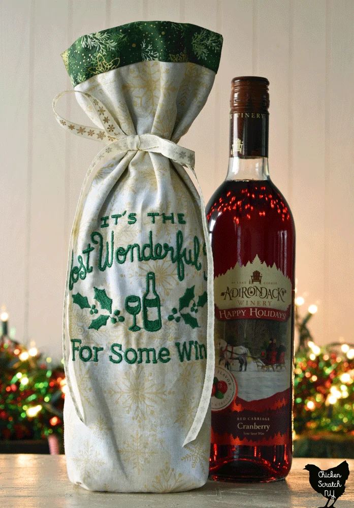 wine bottle bag made from cream snowflake print with green metallic snowflake lining with bottle of red wine next to it