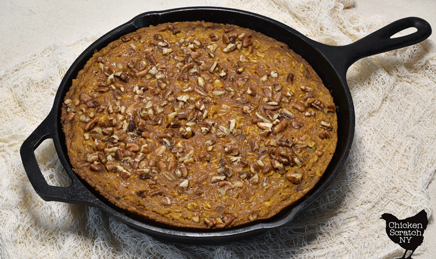 cast iron skillet filled with baked pumpkin oatmeal topped with toasted pecans
