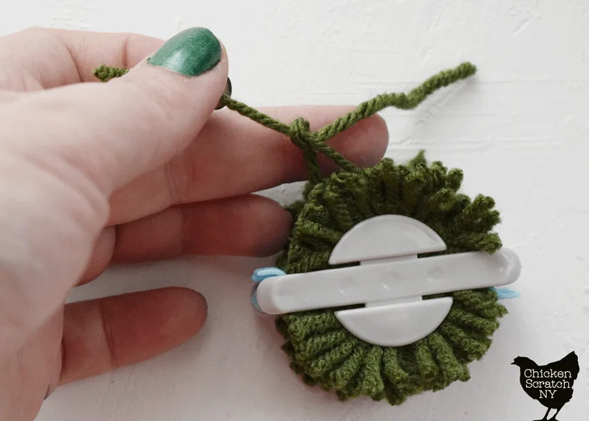 tightly tie a piece of yarn around the center of the pompom maker