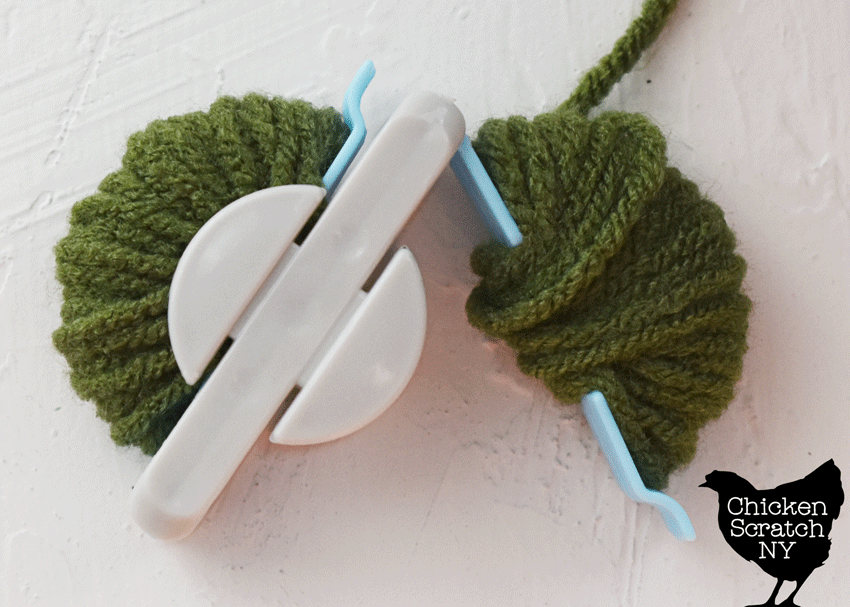 plastic pompom makers wrapped with green yarn showing how to open the maker and how full to wrap it